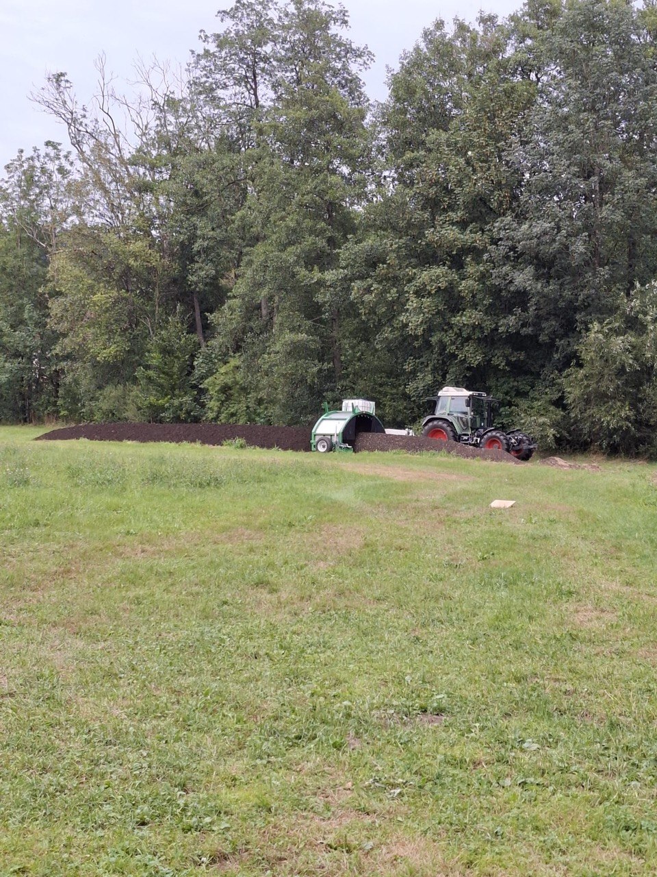Traktor bei der Herstellung von thermisch kontrolliertem Kompost auf einer grünen Wiese